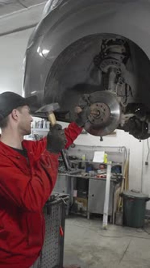 Auto mechanic hits brake disc with hammer during repair at service garage. 4K