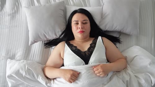 Woman Smiling in Bed Under White Sheets