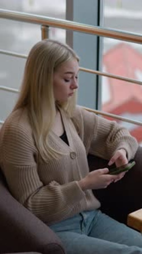 Elegant Woman Seated in Restaurant Looking Thoughtful and Waiting for Someone While Holding Phone