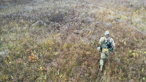 Man in Camouflage Walking Through Grassy Field
