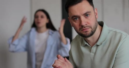 Man Looks at Camera as Woman Argues in Background