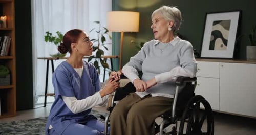 Young Woman Speaks With Senior Woman in Wheelchair