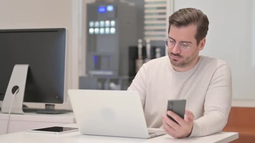 Man Working at Desk Using Phone and Laptop