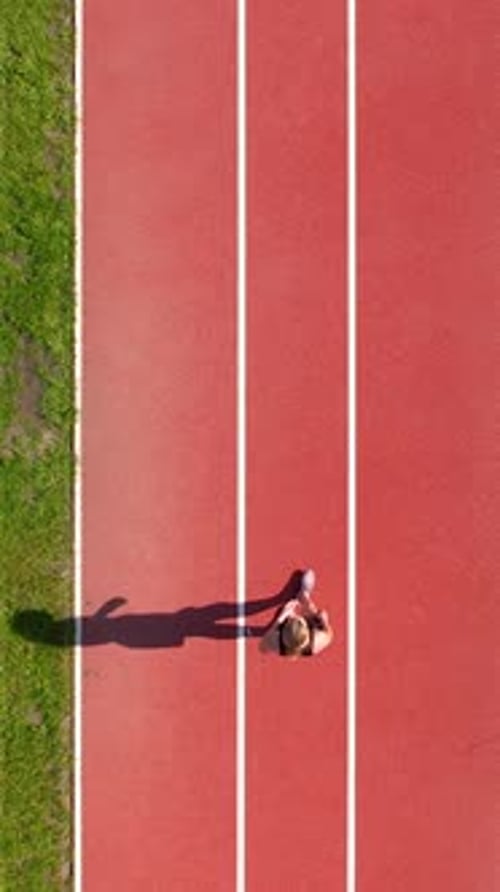 Aerial Top Down View Of Woman Running On Red Athletics Track