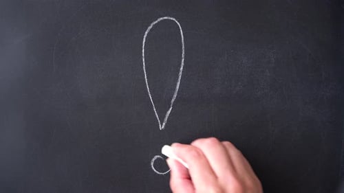 Writing exclamation mark with chalk on blackboard.