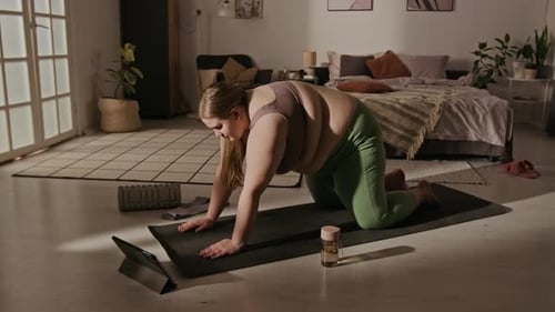 Mujer de talla grande practicando yoga en línea con tableta en casa