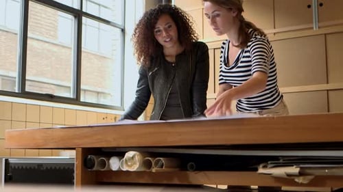 Young Female architects discussing with blueprint in office