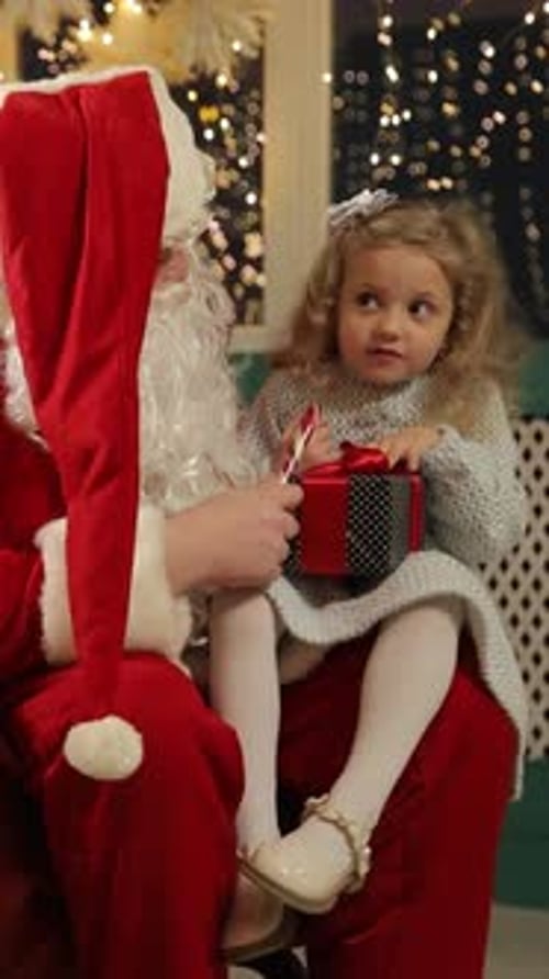 Cute Girl Sitting with Santa Receiving a Gift
