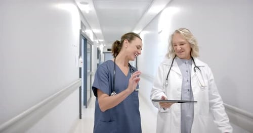 Caucasian female doctors in discussion using tablet in hospital corridor, slow motion