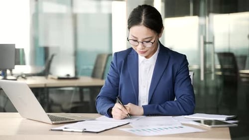 Die vielbeschäftigte junge asiatische Geschäftsfrau füllt Dokumente mit einem Stift aus und sitzt am Arbeitsplatz im Büro.