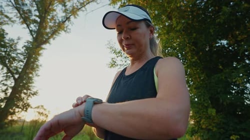 Runner Checks Her Smartwatch During a Sunset Jog in a Serene Park
