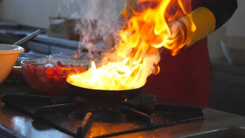 Männlicher Koch, der in der modernen Küche eines Restaurants ein Gericht im Flambenstil auf einer Pfanne zubereitet, professioneller Koch beim Werfen