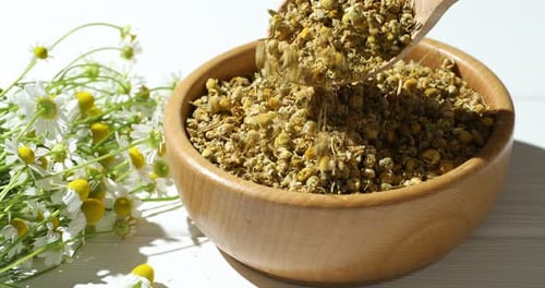 Dried chamomile tea being scooped into bowl.