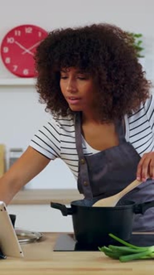Mujer joven cocinando y siguiendo la receta en una tableta digital en la cocina