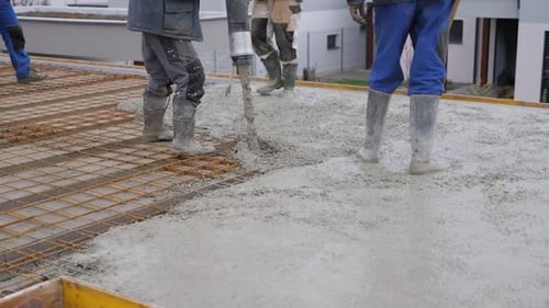 workers building a house, pouring a concrete floor on reinforced steel fences laid down on the roof