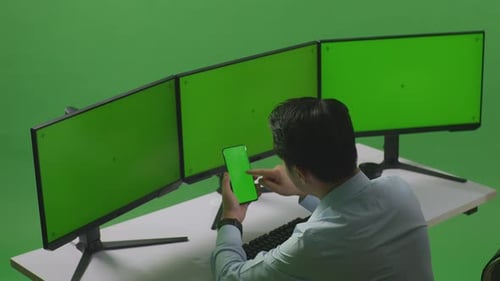 Asian Man Using Mobile Phone And Multiple Computer Monitor With Mock Up Green Screen In Green Screen