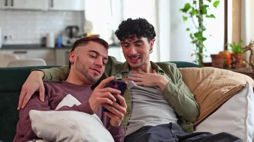 Affectionate Gay Couple Using Smartphone Together on Sofa