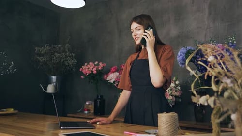 Caucasian Woman Florist Takes an Order in a Flower Shop By Phone Clarifies Details with the Customer