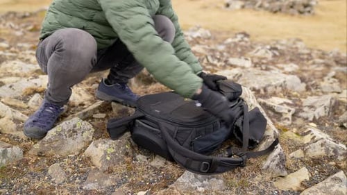 Person Opens Camera Bag Outside on Rocky Ground
