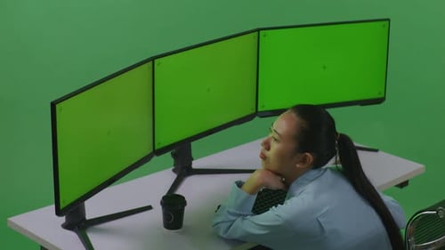 Side View Of Bored Asian Woman Working With Mock Up Multiple Computer Monitor In Green Screen