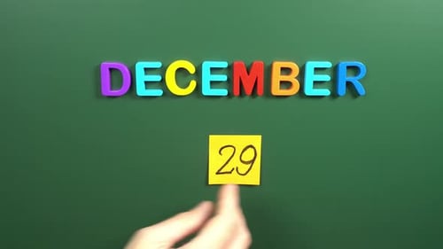 Hand sticking a sticker 29 December calendar day on school board. 29 date of December. Twenty