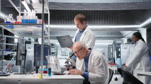 Cientista idoso usando microscópio com um colega para estudo clínico