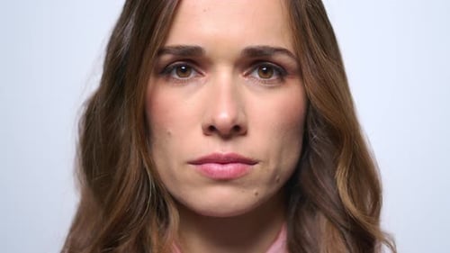 Serious young woman face portrait on blue background in studio close up
