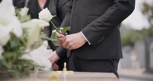 Hand, rose and a person at a funeral in a graveyard in grief while mourning loss at a memorial