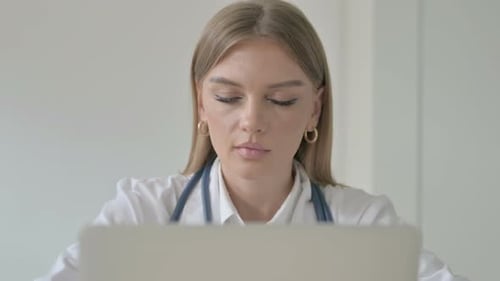 Close Up of Female Doctor Smiling at Camera While Working on Laptop in Clinic