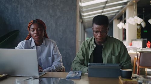 Two Black Business Partners One Male and One Female are in the Midst of Negotiations at a Cafe Using