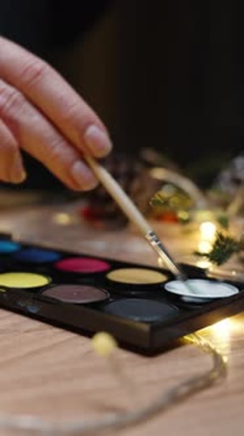 Vertical video. A young woman is preparing decorations for the New Year, painting pinecones