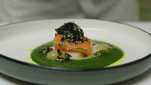 Close up shot of professional chef in luxury restaurant adding greens on fancy served salmon plate