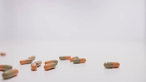 Medikamentenkapseln fallen in Zeitlupe auf weißen Hintergrund.