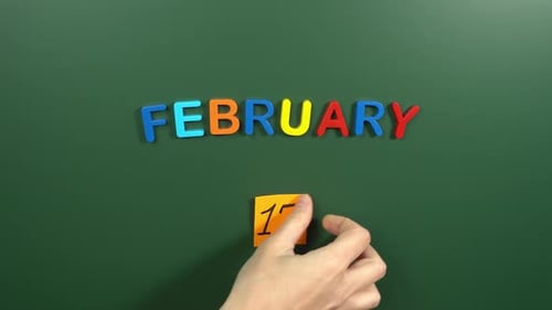 Hand sticking a sticker 17 February calendar day on school board. 17 date of February. Seventeenth