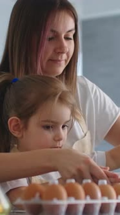 Mother and Daughter Bonding in a Bright Kitchen While Breaking Eggs and Whisking Batter Together for