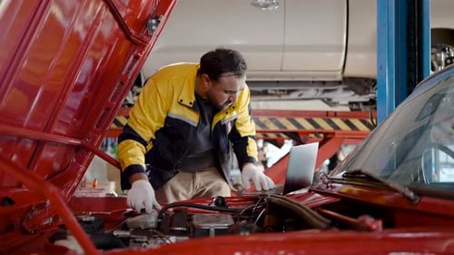 Mechanic Asian man wear uniform using computer laptop examining tuning fixing repairing car engine