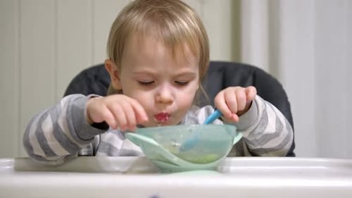 Child Eating Food With Spoon and Hands