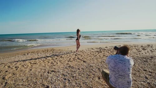 Un photographe masculin photographie une femme sur un bord de mer sablonneux