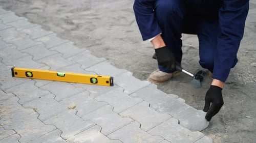 Trabajador instalando adoquines con un mazo y una herramienta niveladora