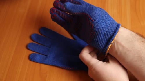Man Putting On Blue Working Gloves on Table