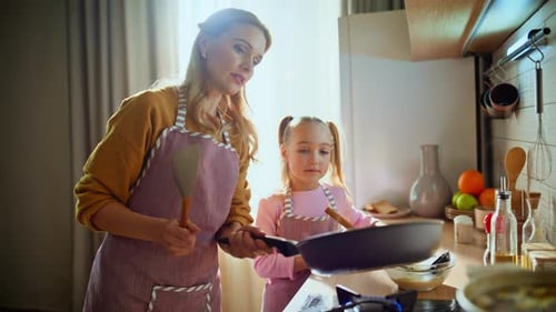 Caring Mom Teaching Daughter to Cook Pancakes Standing Sunny Kitchen Closeup