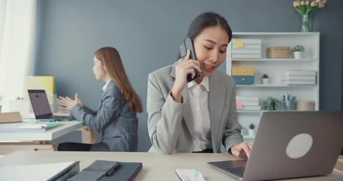 Asia businesswomen talking on mobile phone and communicate sitting on office desk at workplace.