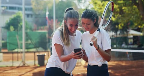 Women Laughing at Phone on Tennis Court