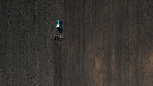 Top View of a Tractor with Harrow System Plowing Ground on Cultivated Farm Field