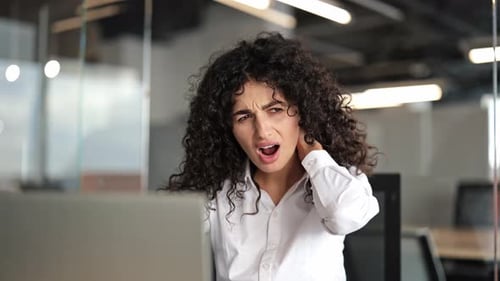 Tired Businesswoman Massages Neck While Working on Laptop in Office