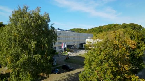 Aerial dolly forward drone shot of modern university building facade with sunny trees
