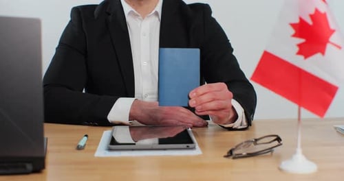 Person Holds Passport at Desk with Canadian Flag