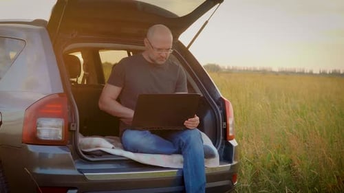 Concentre-se em um freelancer masculino confiante trabalhando no laptop Homem digitando no teclado sentado no porta-malas do carro