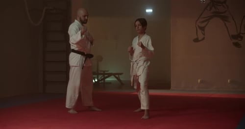 Young Karate Student Kicks Air Under Guidance of Sensei in Gym