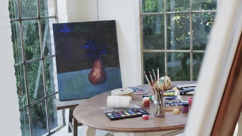 Close up of paintings on easels and paints and brushes on table in studio, slow motion
